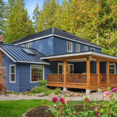 Custom home addition with blue exterior siding, standing-seam metal roofing, and a covered cedar deck surrounded by Pacific Northwest landscaping.